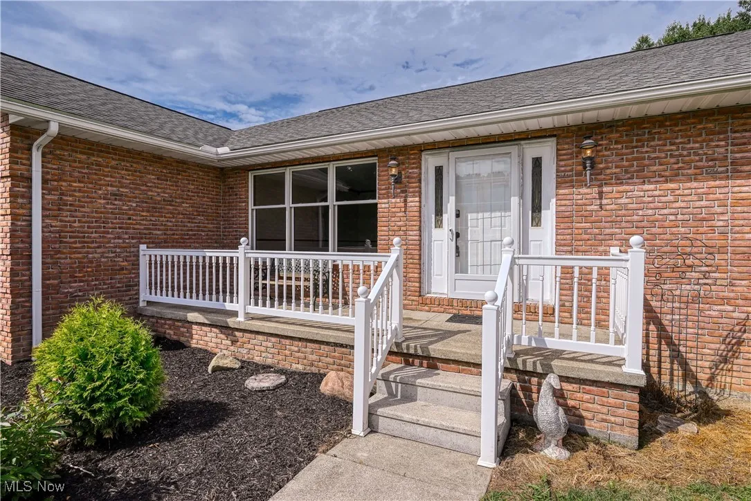 View of exterior entry with brick siding and a shingled roof