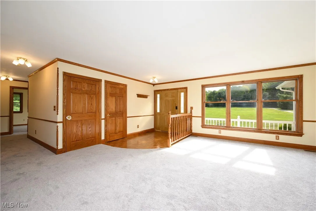 Unfurnished living room featuring healthy amount of natural light, light colored carpet, crown molding, and a water view