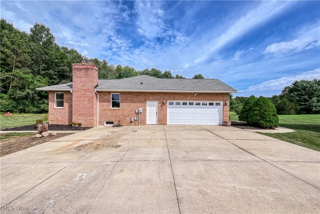 View of home's exterior featuring brick siding, concrete driveway, a chimney, roof with shingles, and a garage