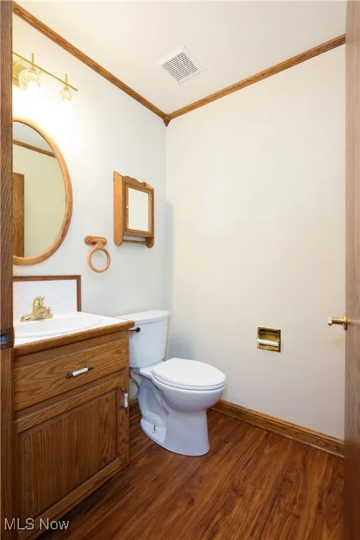 Half bathroom with crown molding, vanity, and wood finished floors