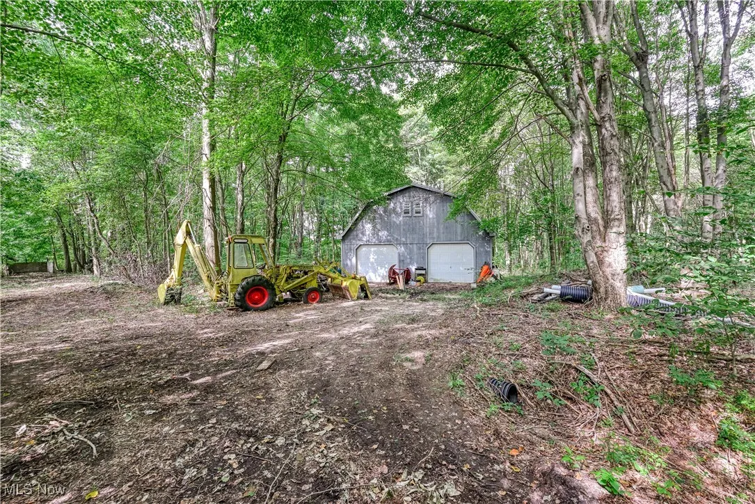 View of yard featuring an outbuilding, a detached garage, dirt driveway, and a wooded view