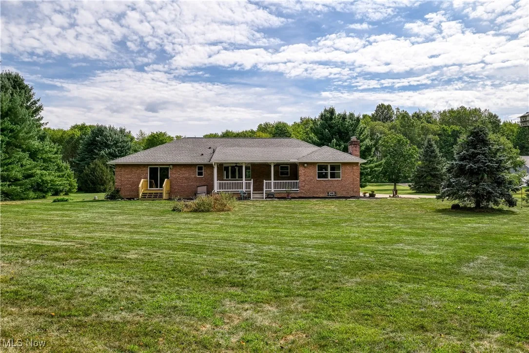 Rear view of house featuring covered porch, brick siding, a chimney, and a lawn