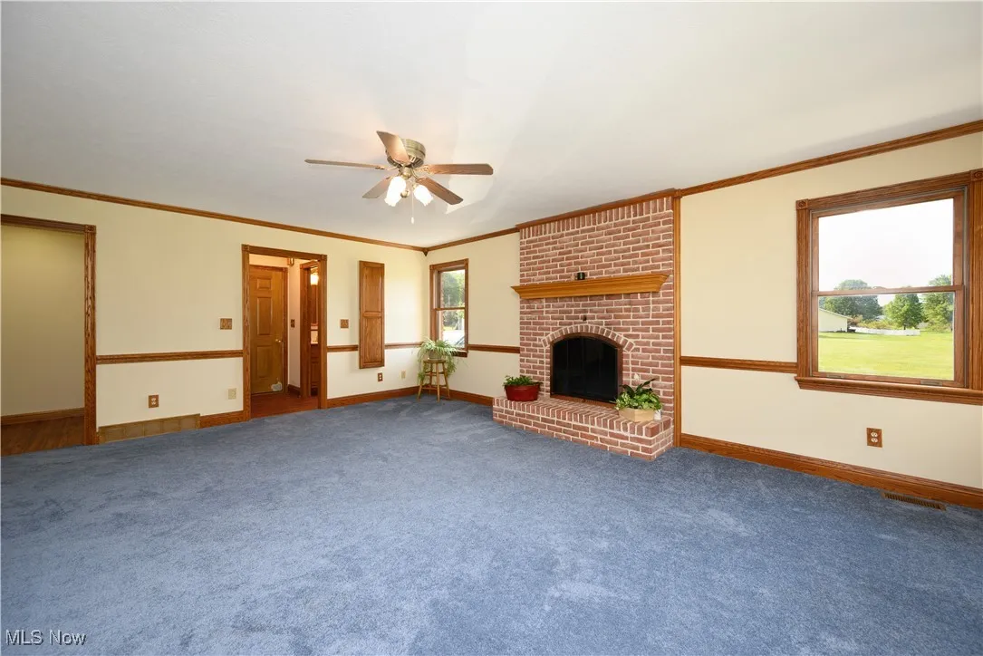 Unfurnished living room featuring crown molding, a fireplace, carpet, and ceiling fan