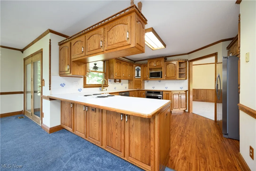 Kitchen with crown molding, brown cabinets, light countertops, a peninsula, and stainless steel appliances