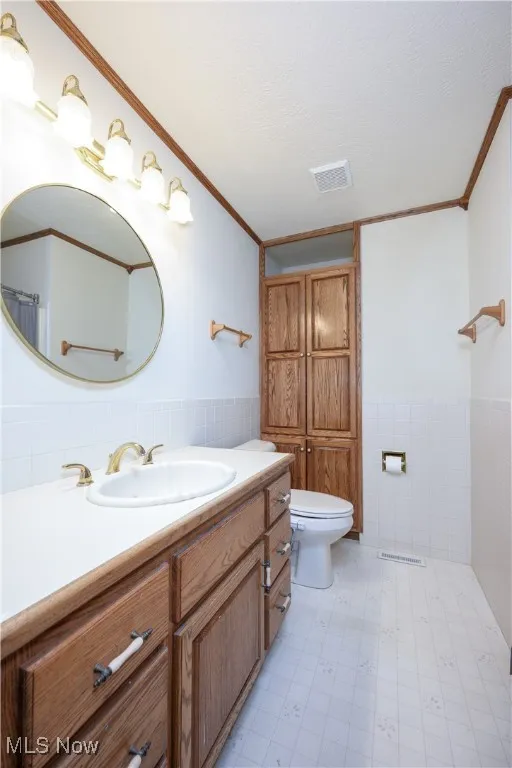 Bathroom featuring tile walls, a wainscoted wall, vanity, ornamental molding, and a textured ceiling