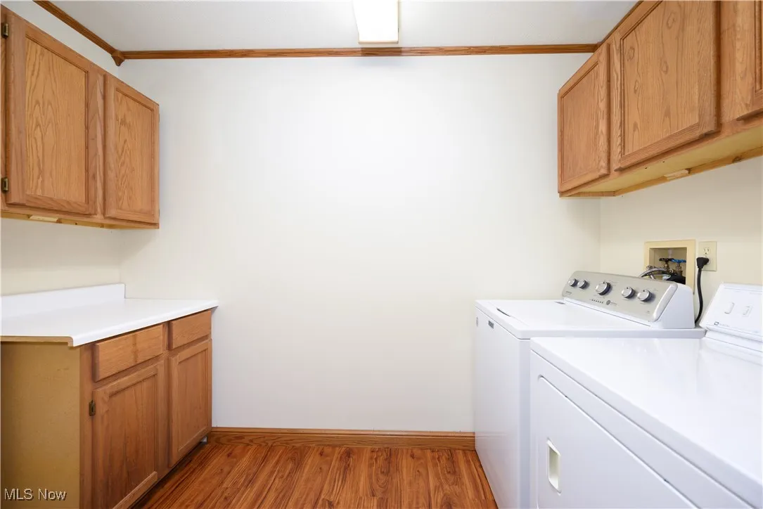 Laundry room with cabinet space, light wood-type flooring, ornamental molding, and separate washer and dryer