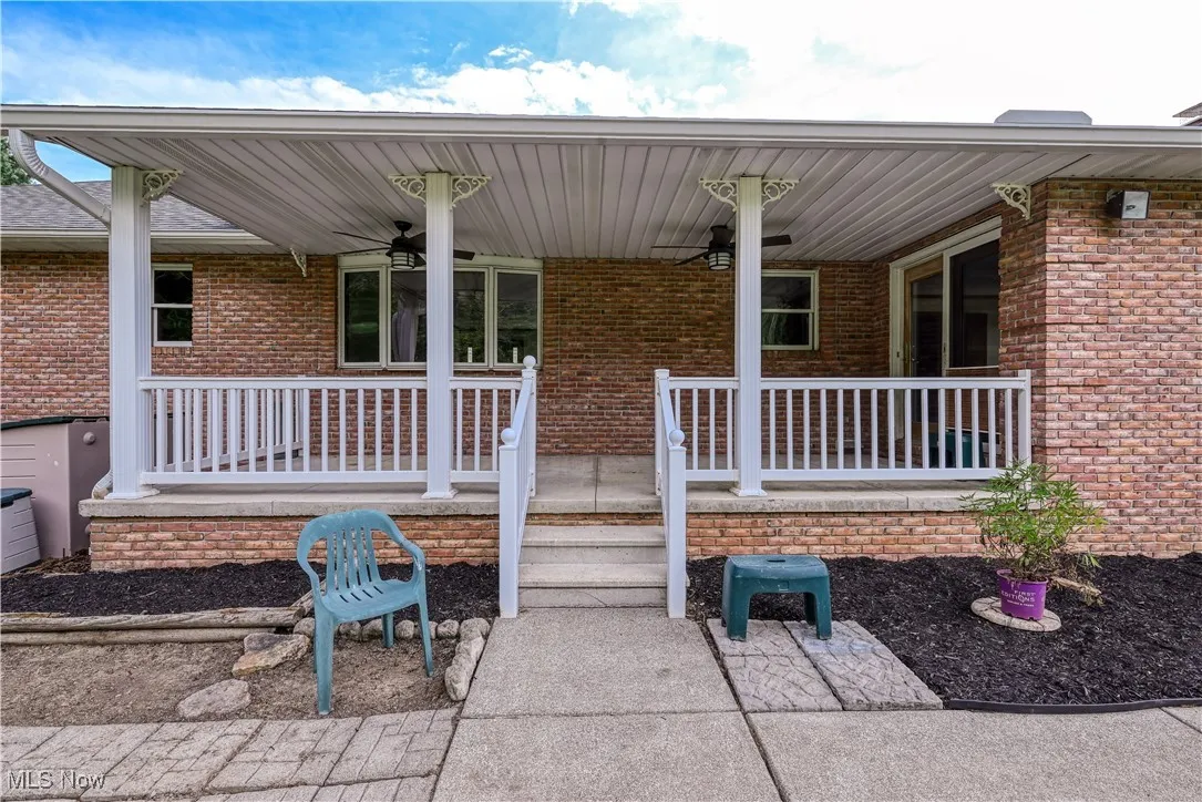 Entrance to property with ceiling fan, a porch, and brick siding