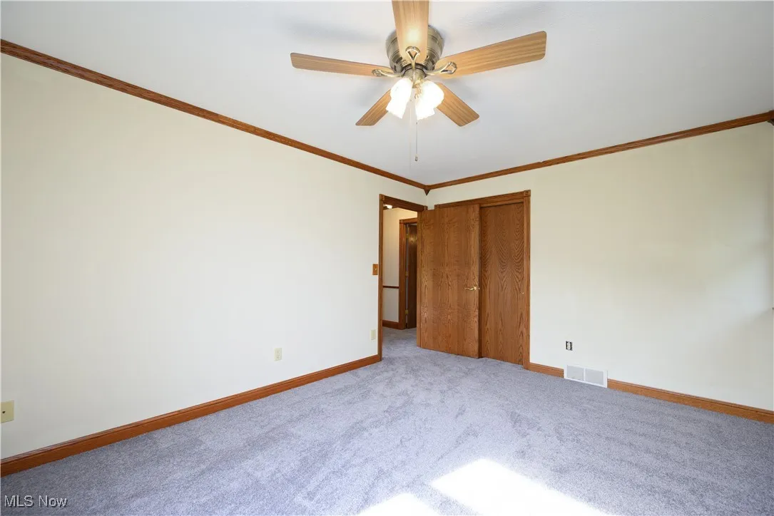 Unfurnished bedroom with carpet flooring, crown molding, ceiling fan, and a closet