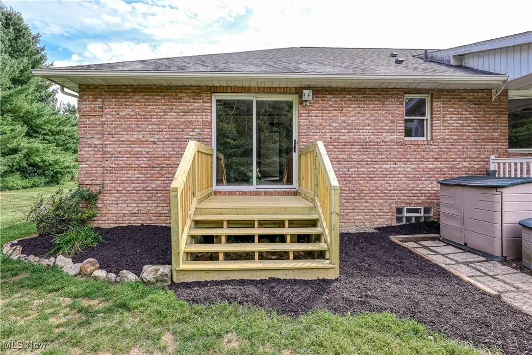 Back of property featuring a deck, brick siding, and roof with shingles