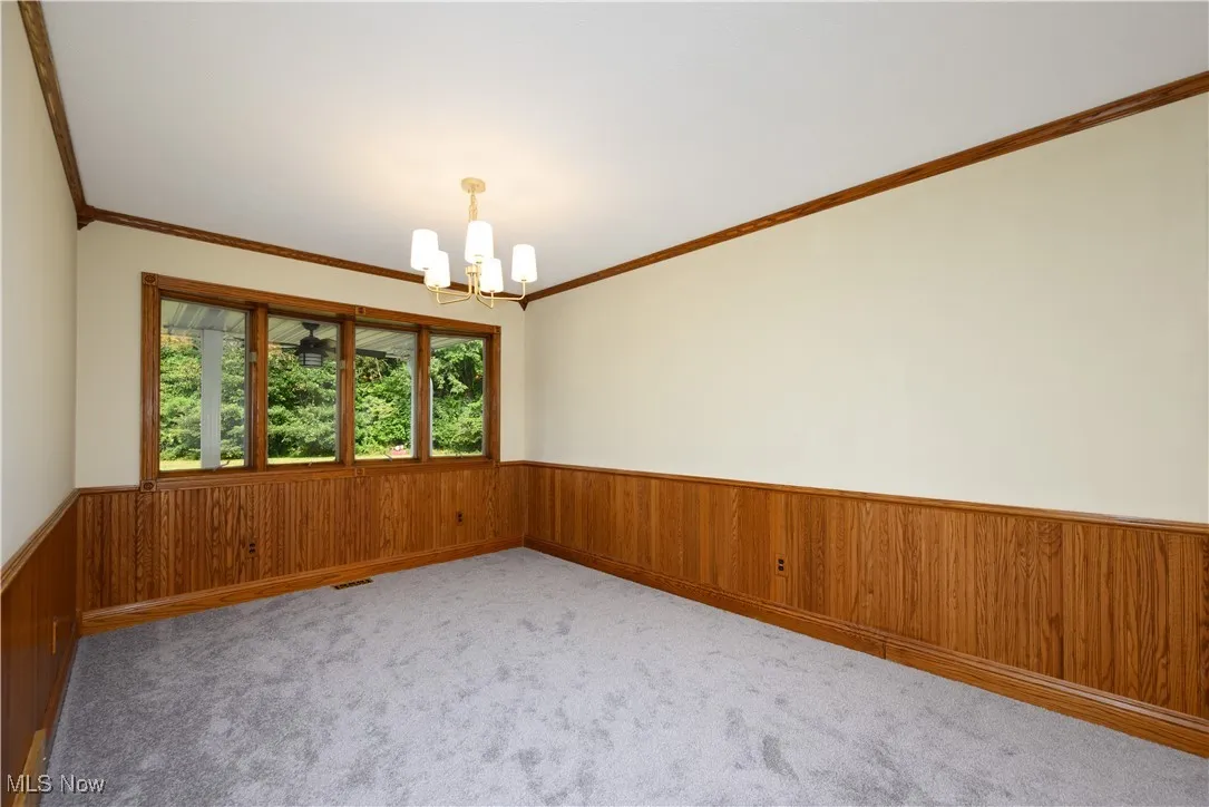 Unfurnished room featuring a chandelier, wood walls, crown molding, wainscoting, and carpet flooring