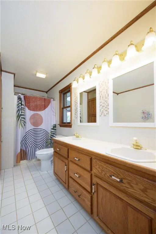 Bathroom featuring double vanity, light tile patterned flooring, crown molding, tile walls, and curtained shower