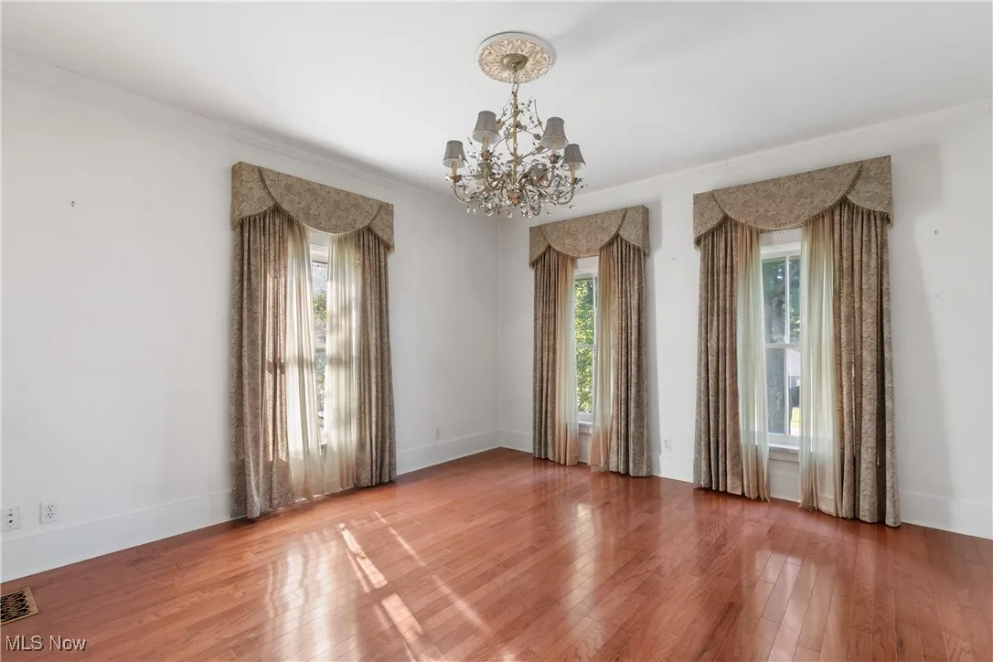Unfurnished room featuring hardwood / wood-style floors, a chandelier, and ornamental molding