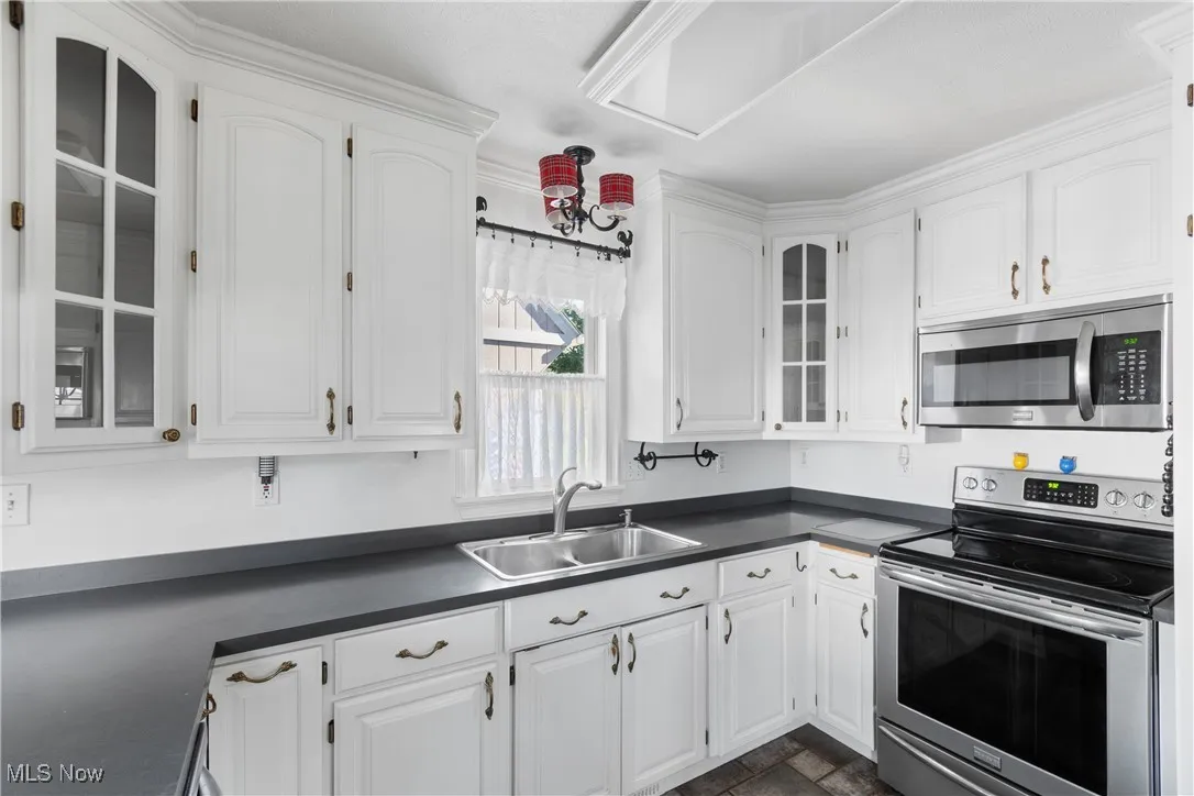 Kitchen featuring glass insert cabinets, appliances with stainless steel finishes, dark countertops, and white cabinetry
