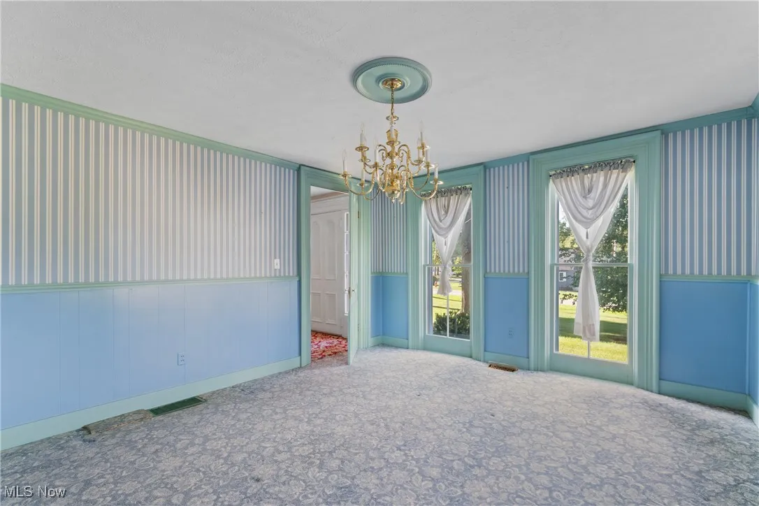 Empty room featuring a chandelier, carpet flooring, and wainscoting