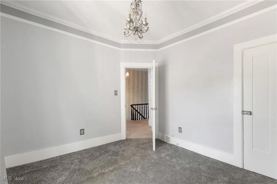 Spare room with ornamental molding, a chandelier, and carpet floors