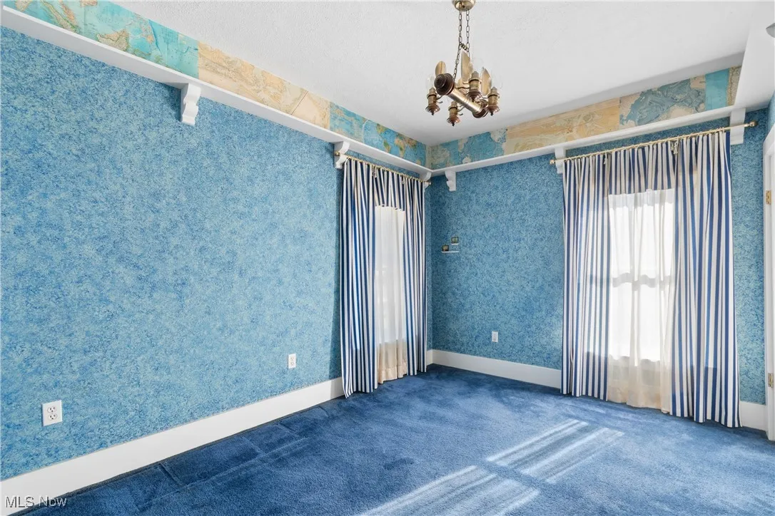 Carpeted spare room with wallpapered walls and a chandelier