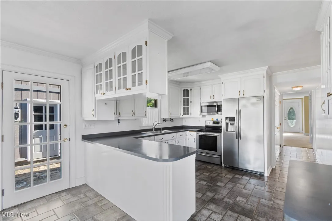 Kitchen featuring stainless steel appliances, a peninsula, white cabinets, crown molding, and dark stone finish floors
