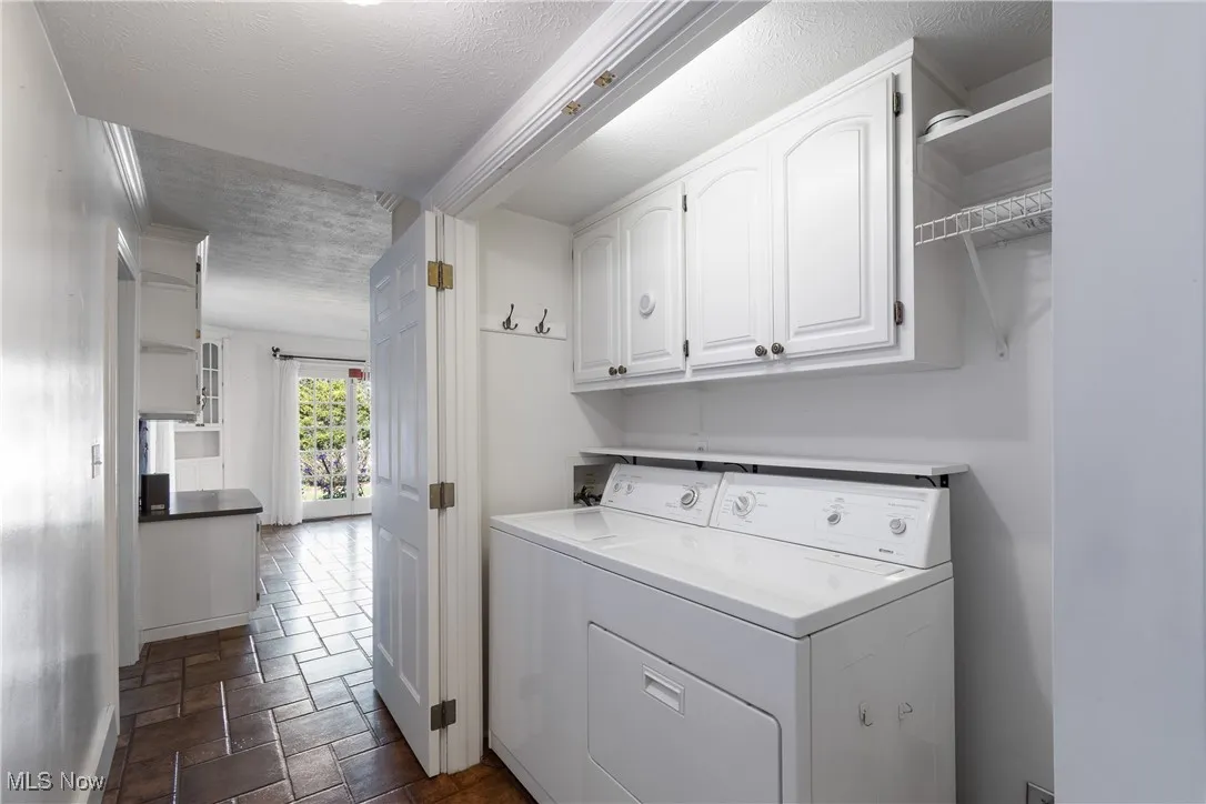 Laundry area featuring a textured ceiling, cabinet space, dark stone finish floors, and separate washer and dryer