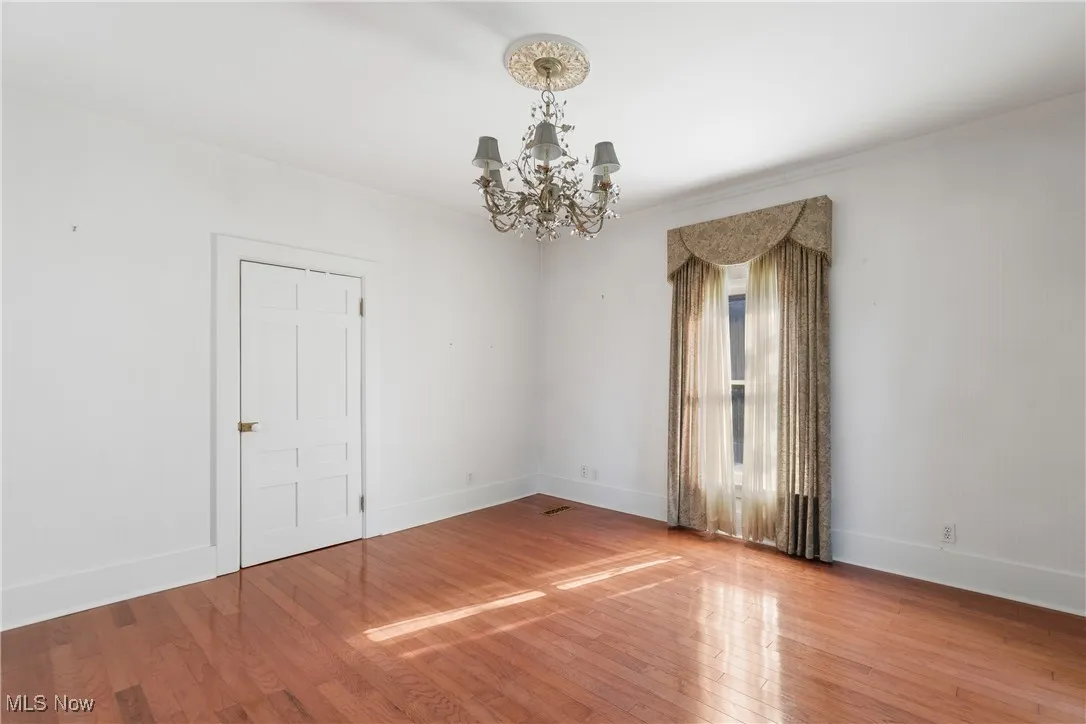 Spare room featuring wood-type flooring, ornamental molding, and a chandelier