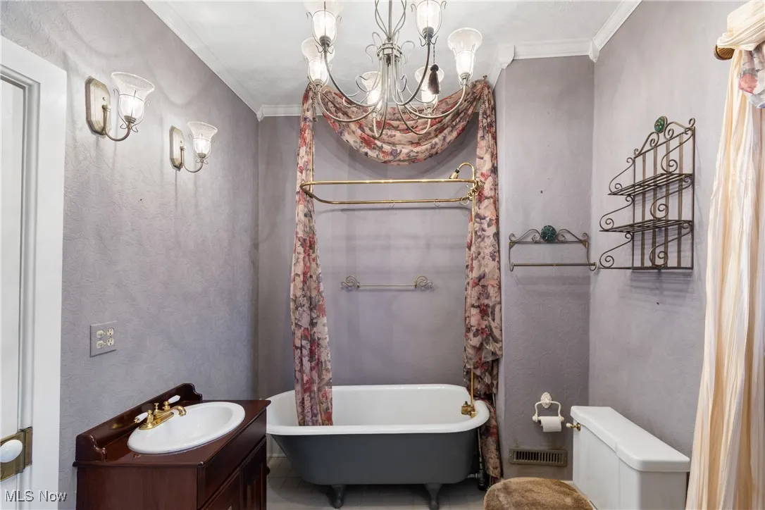 Full bath with a soaking tub, vanity, ornamental molding, a chandelier, and a textured wall