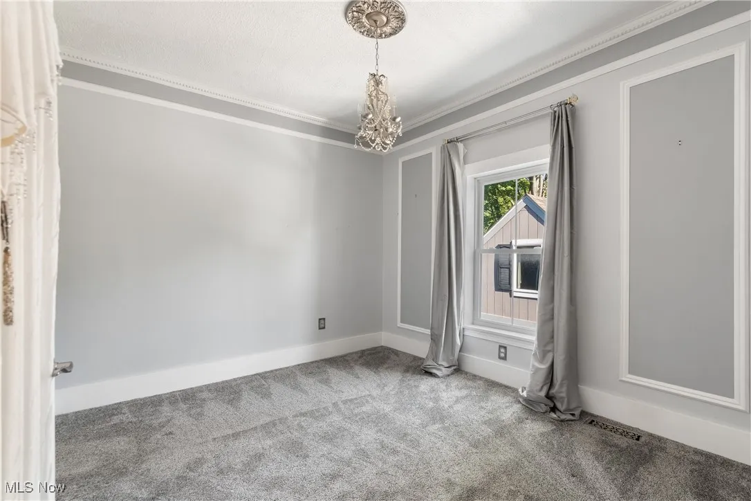 Carpeted empty room with ornamental molding and a chandelier