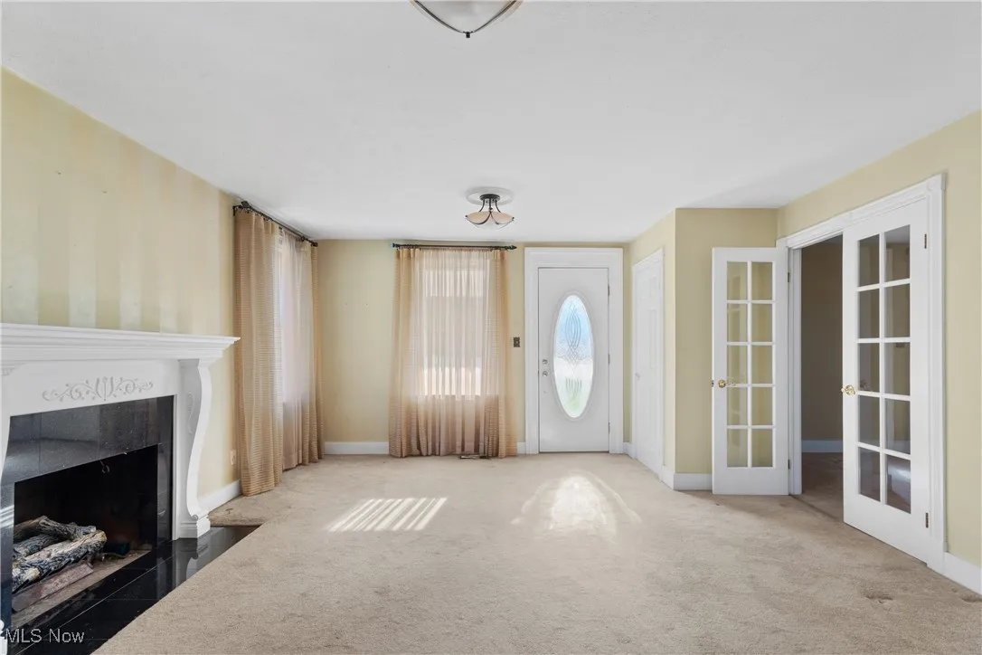 Unfurnished living room featuring french doors, carpet flooring, and a fireplace
