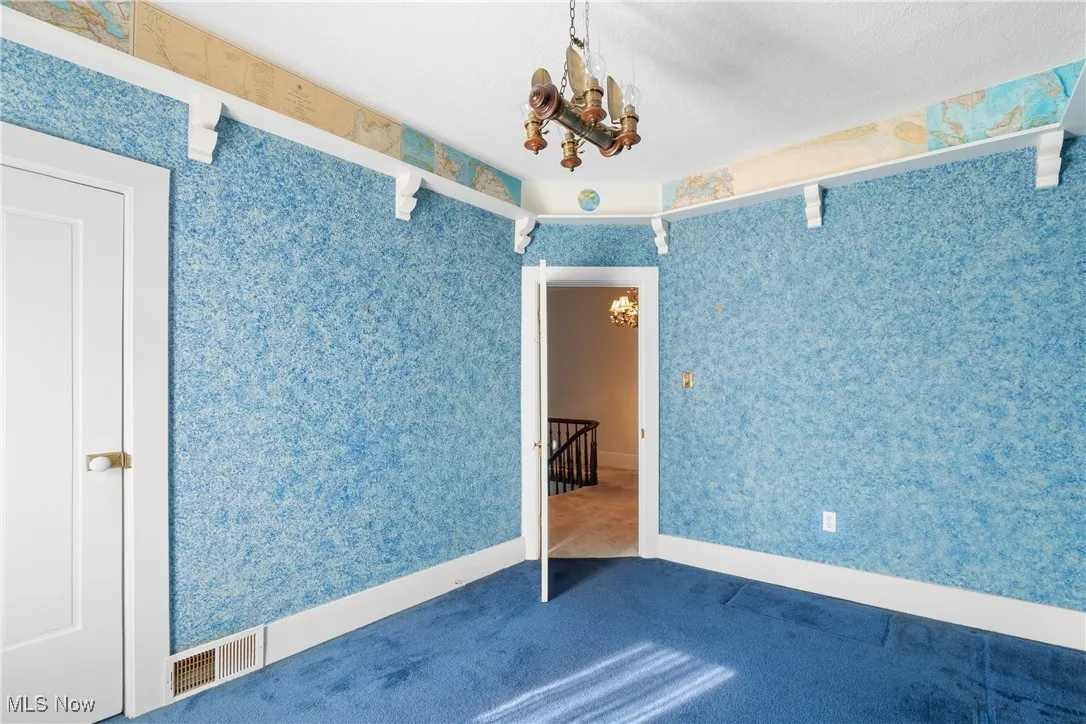 Carpeted spare room featuring a chandelier and wallpapered walls
