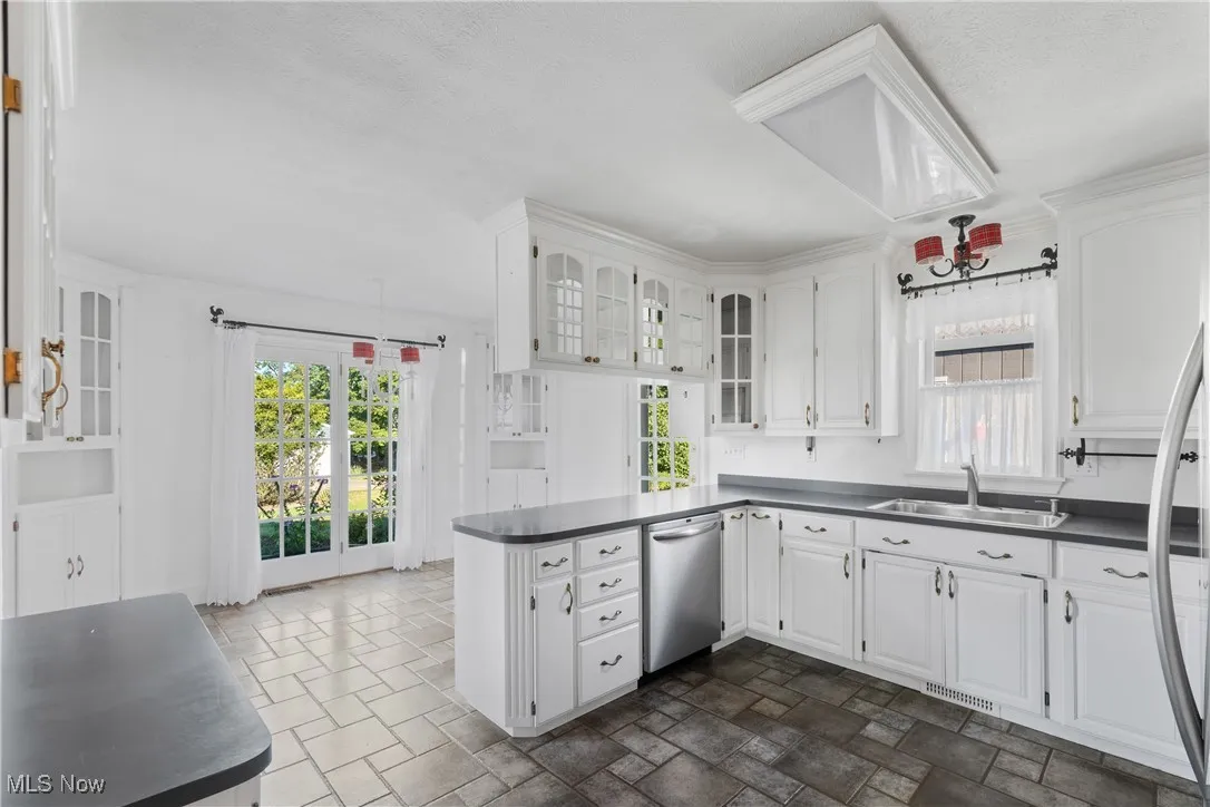 Kitchen with glass insert cabinets, white cabinets, dark countertops, and stone finish flooring
