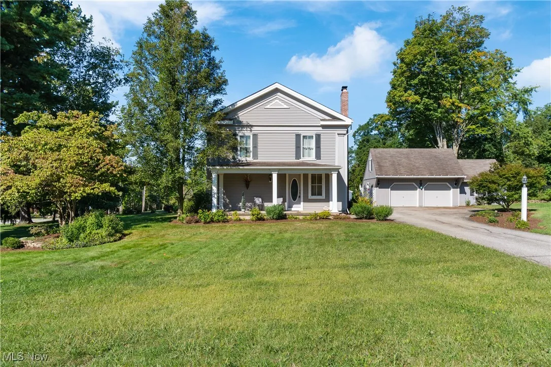 Greek revival house with covered porch, a chimney, a front yard, and a garage