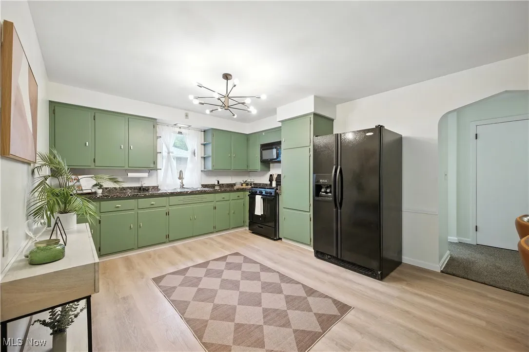 Kitchen with green cabinets, black appliances, light wood-style flooring, arched walkways, and a chandelier