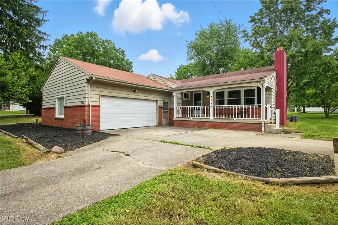 Ranch-style house with driveway, brick siding, a chimney, an attached garage, and covered porch