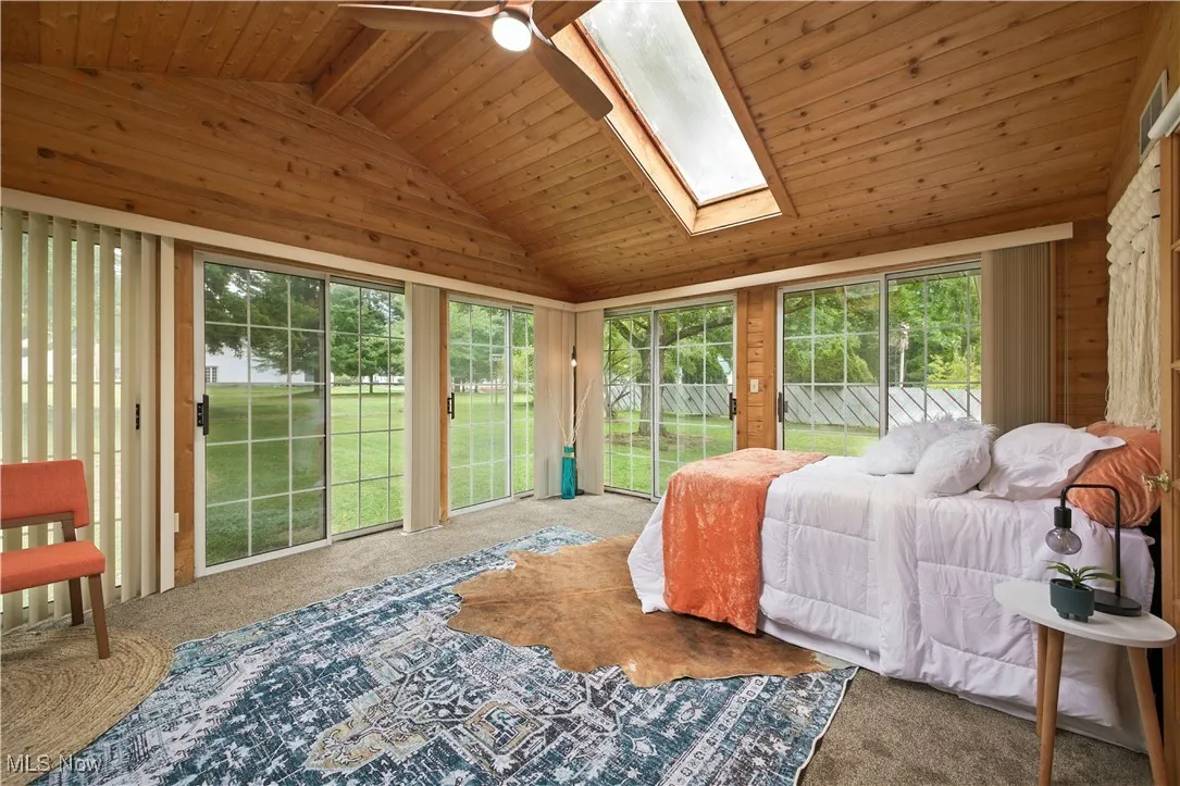 Bedroom with access to outside, wooden ceiling, carpet, a skylight, and a ceiling fan
