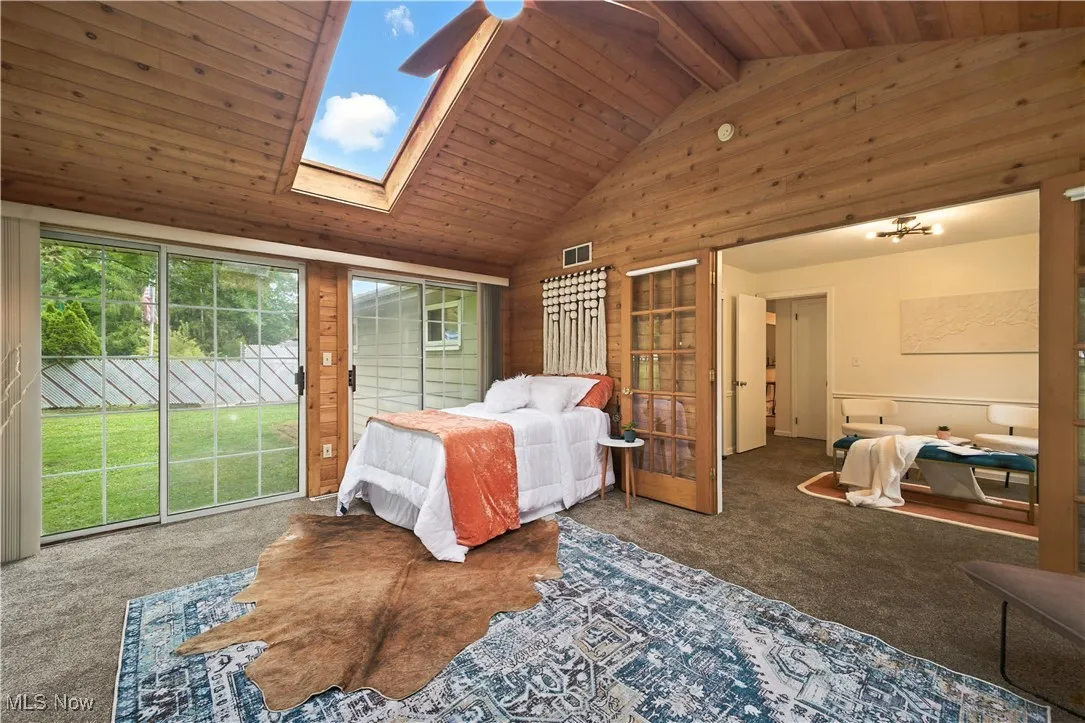 Bedroom with a wood ceiling with exposed beams, carpet floors, a skylight, access to outside, and high vaulted ceiling