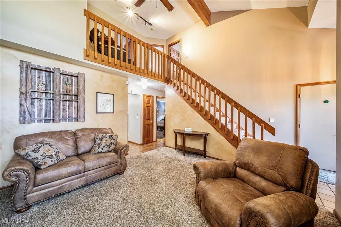 Living area with beamed ceiling, stairs, a ceiling fan, high vaulted ceiling, and carpet