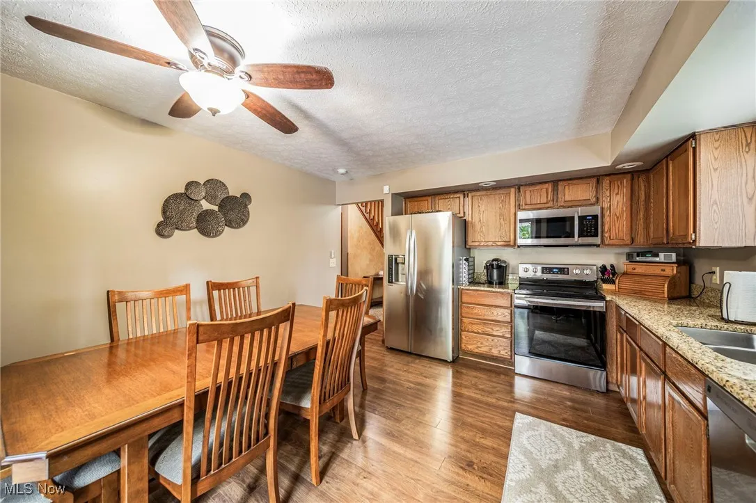 Kitchen with a textured ceiling, stainless steel appliances, brown cabinetry, dark wood-style floors, and light stone countertops
