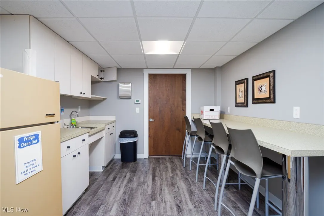 Kitchen with freestanding refrigerator, light countertops, dark wood finished floors, a kitchen breakfast bar, and a drop ceiling