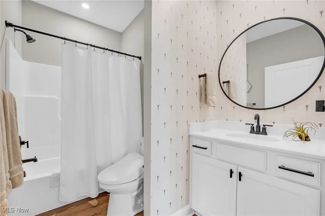 Bathroom featuring wallpapered walls, vanity, shower / bath combo with shower curtain, and light wood finished floors