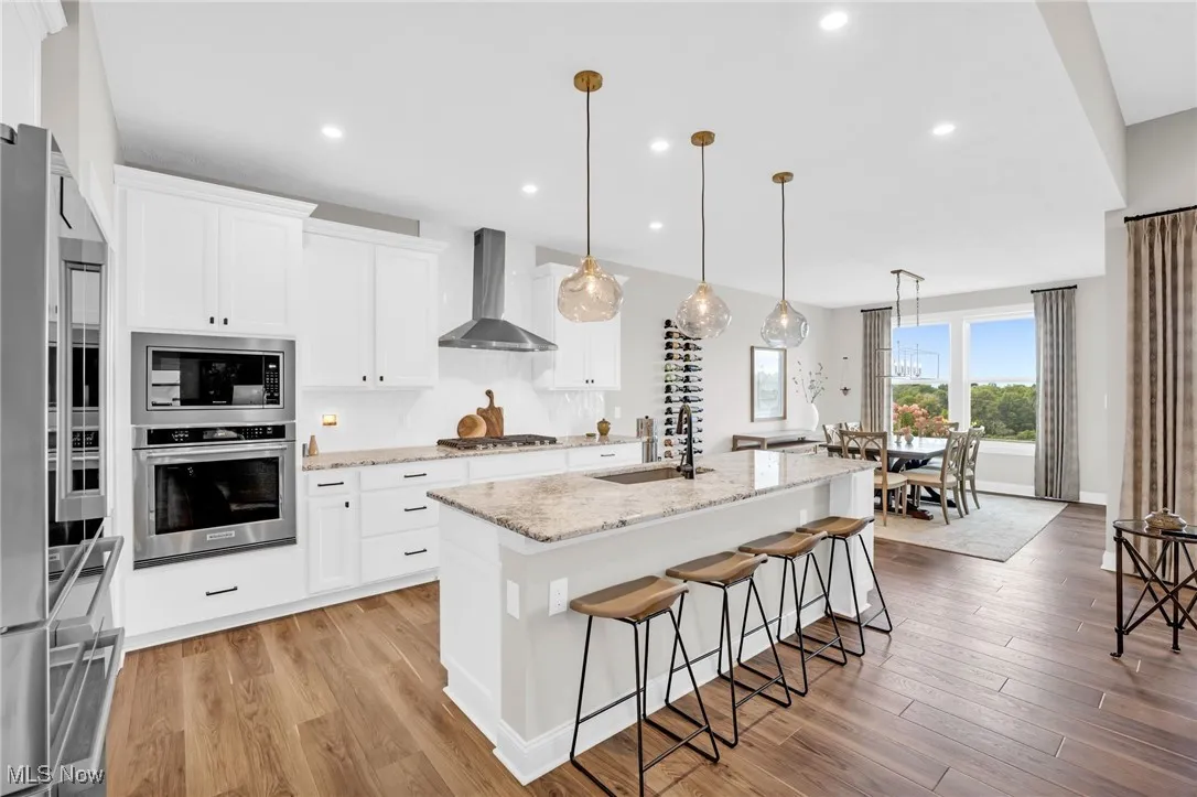 Kitchen featuring a kitchen island with sink, appliances with stainless steel finishes, decorative light fixtures, light wood-style floors, and light stone counters