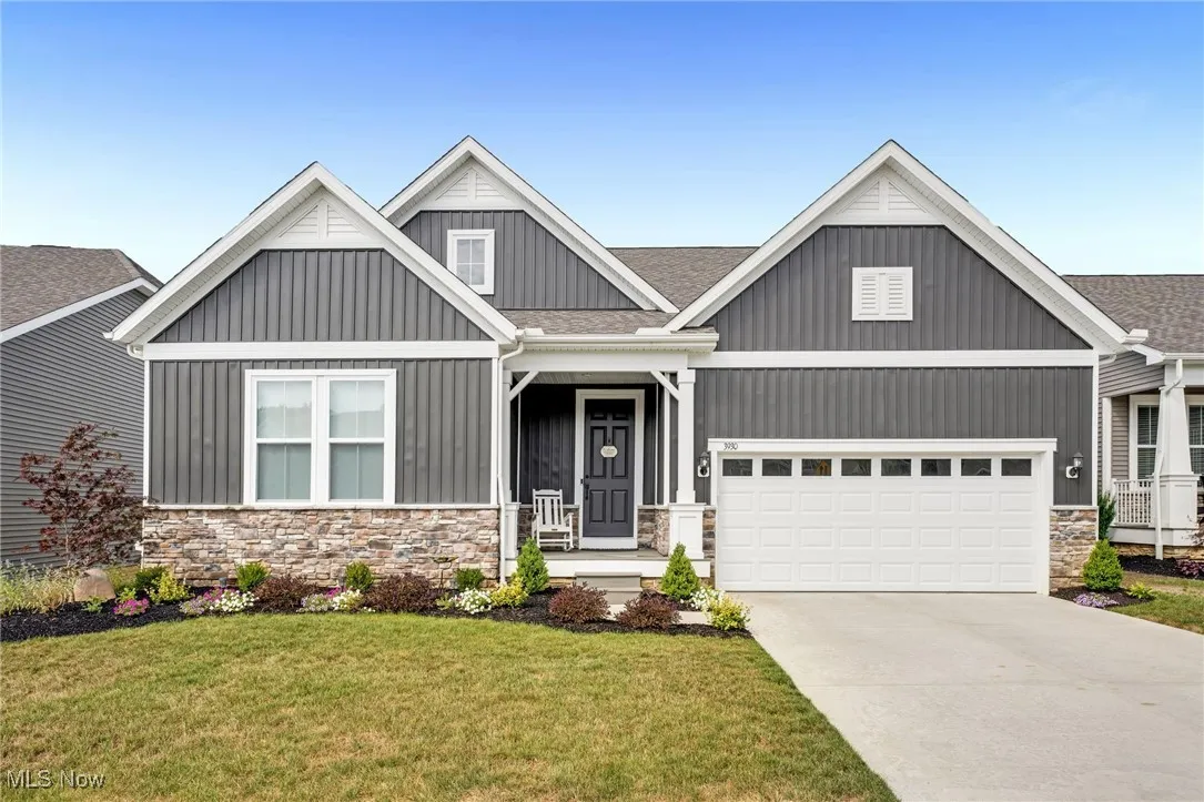 Craftsman-style house with stone siding, board and batten siding, a front lawn, concrete driveway, and roof with shingles