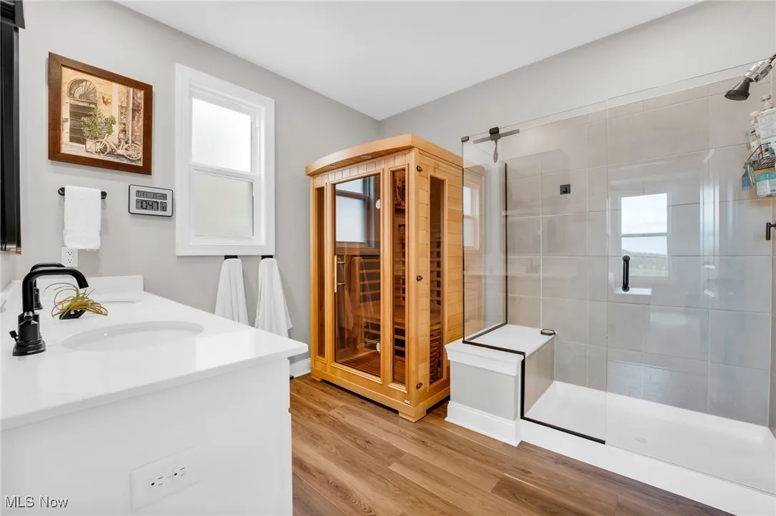 Full bath with a relaxing sauna, a stall shower, double vanity, and light wood-style floors