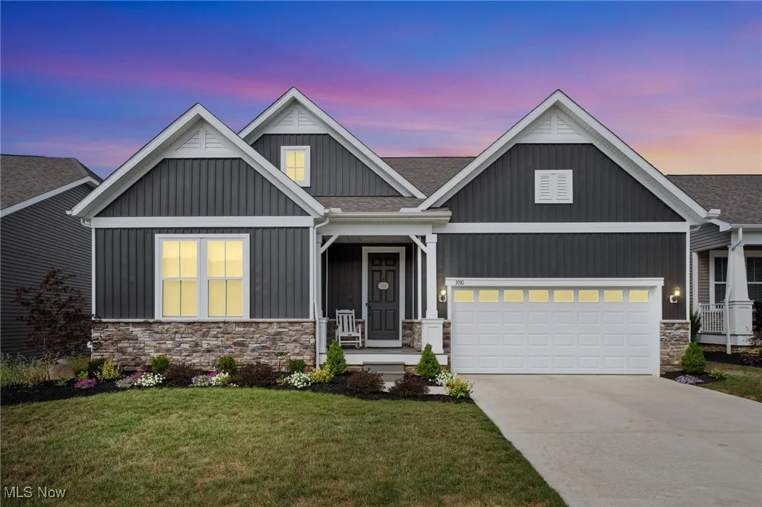 View of front facade with stone siding, driveway, board and batten siding, a front yard, and covered porch