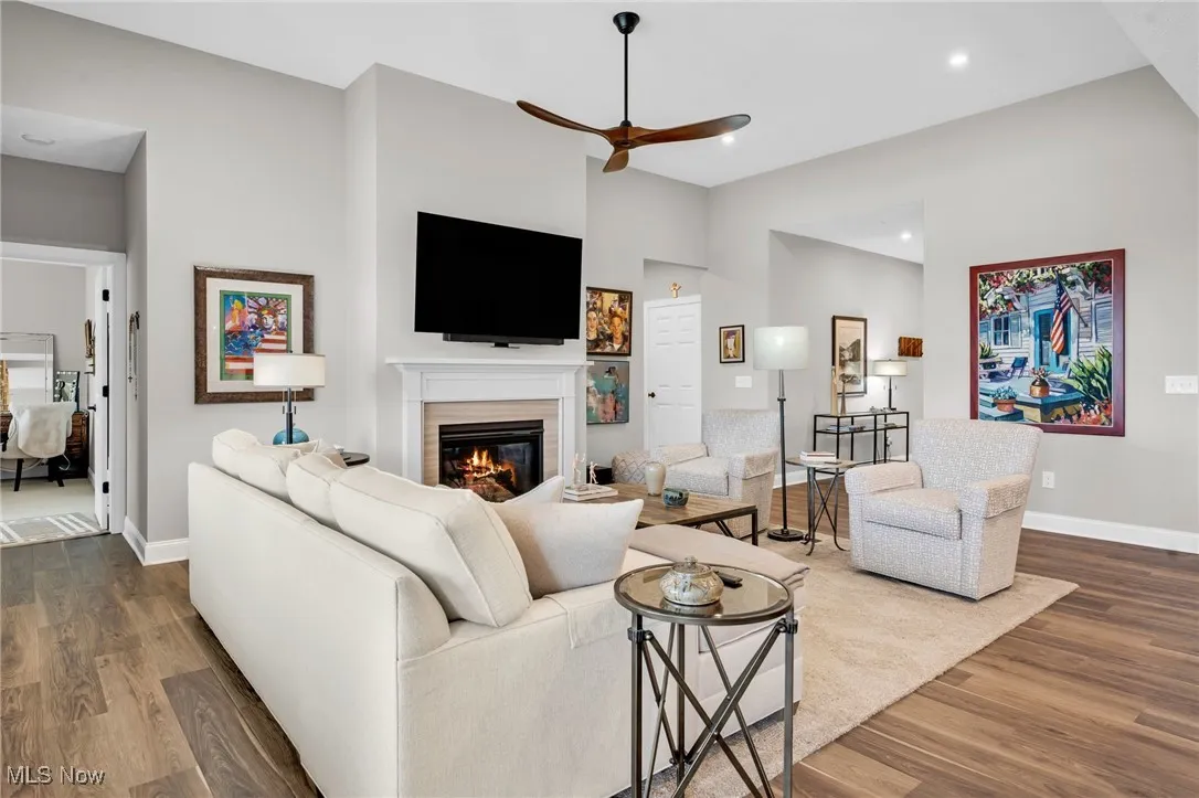 Living area with dark wood-style flooring, a glass covered fireplace, a ceiling fan, and recessed lighting