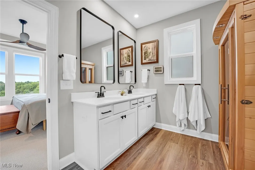 Ensuite bathroom featuring plenty of natural light, double vanity, light wood-style floors, and a sauna / steam room