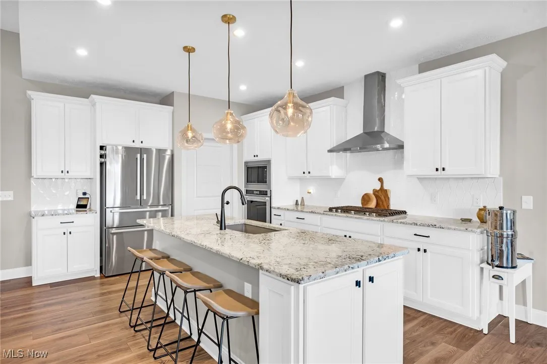 Kitchen with decorative backsplash, stainless steel appliances, light stone counters, white cabinets, and recessed lighting