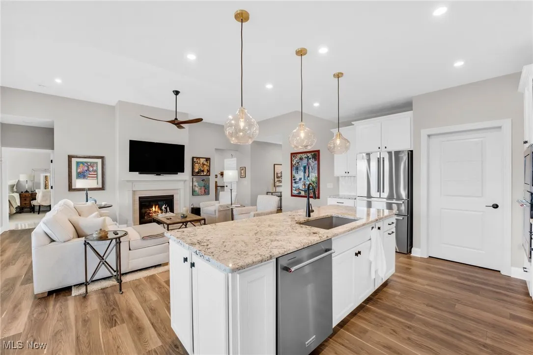 Kitchen featuring white cabinets, stainless steel appliances, decorative light fixtures, ceiling fan, and light stone counters