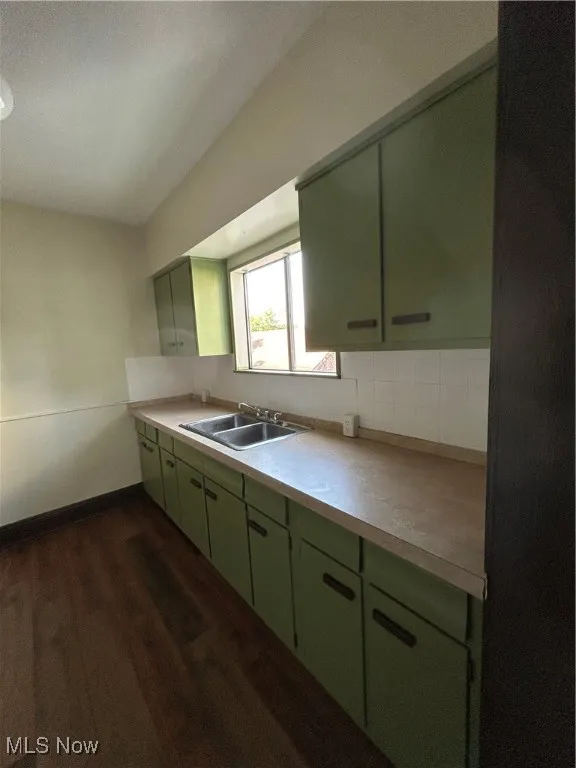 Kitchen featuring green cabinets, dark wood-type flooring, light countertops, and backsplash