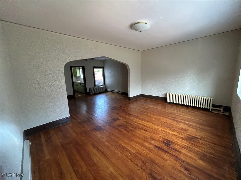 Spare room featuring a textured wall, dark wood finished floors, radiator, arched walkways, and a baseboard radiator