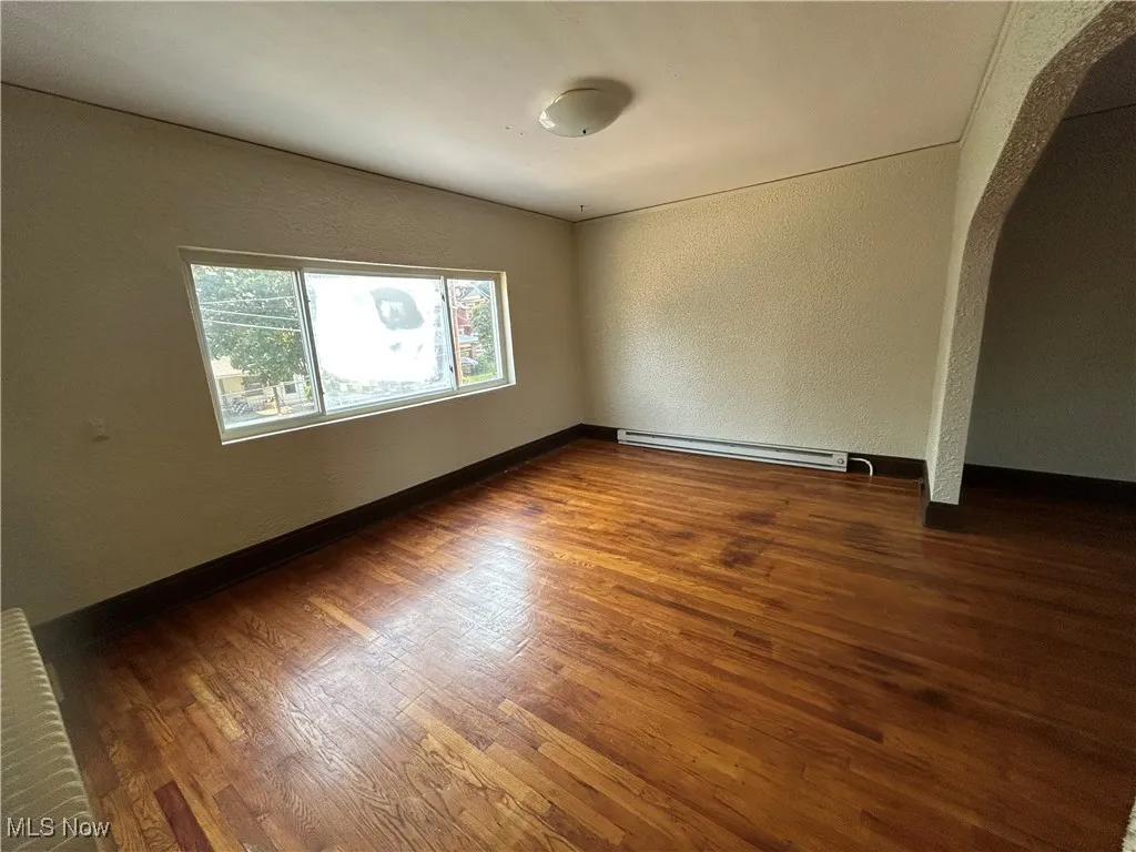 Unfurnished room with a textured wall, arched walkways, wood finished floors, and baseboard heating
