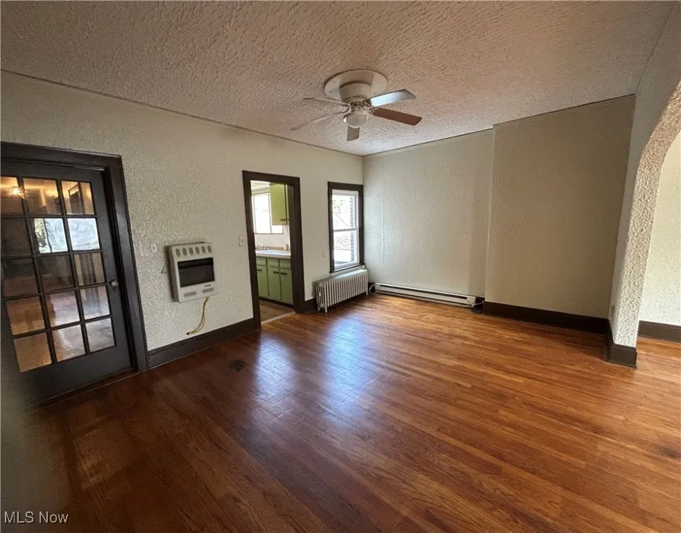 Unfurnished living room with a textured wall, a textured ceiling, dark wood finished floors, radiator heating unit, and heating unit