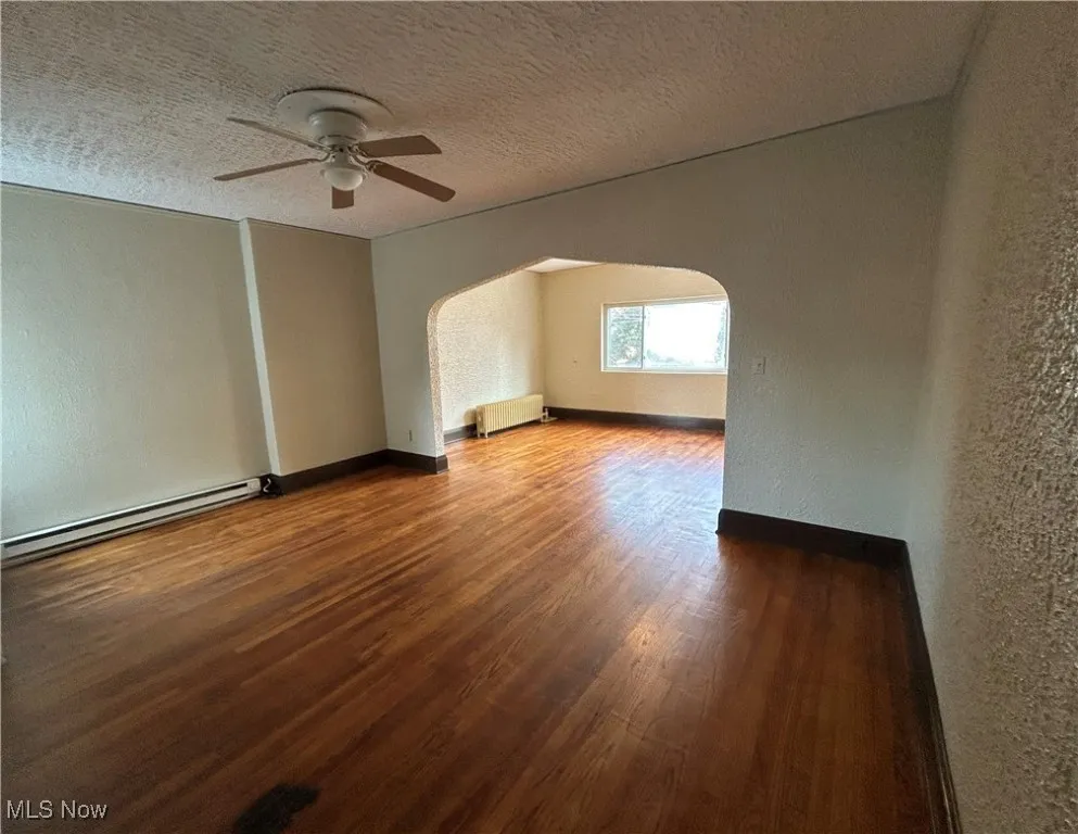 Additional living space with a textured wall, a textured ceiling, arched walkways, wood finished floors, and a baseboard heating unit